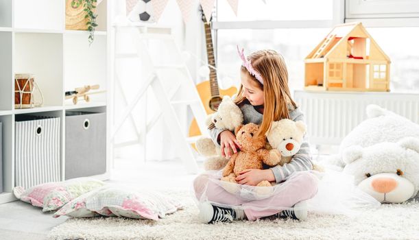 Pretty little girl holding plush teddies in bright children room