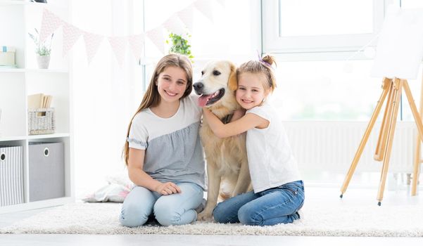 Happy girls friends hugging lovely golden retriever dog in kids room