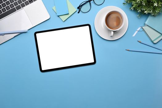 Top view digital tablet, coffee cup, sticky notes and laptop on blue background.