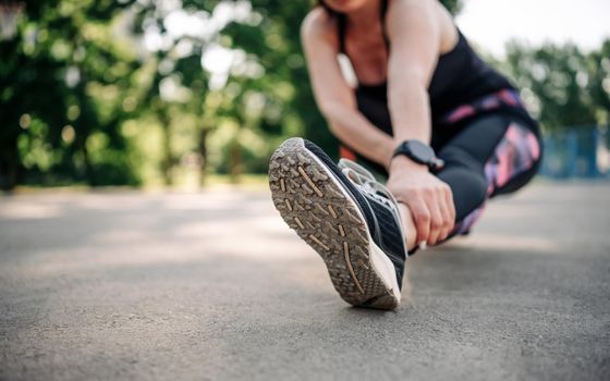 Young girl woman doing stretching outdoors preparing for active fitness workout. Closeup view on leg during training. Female sportsman exercising at stadium outside in summer time