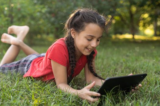 Girl on the grass with a tablet chat in her hands in the garden.