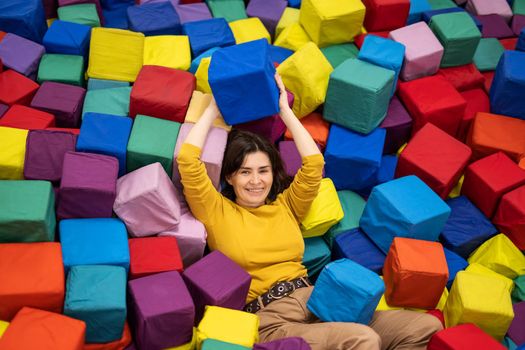 Pretty girl lying on trampoline and holding colorful cube. Young woman enjoying entertaiments at playground park