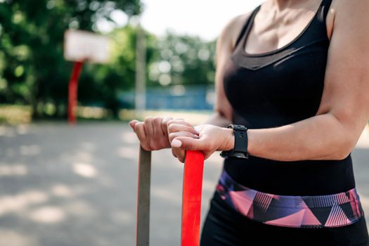 Young girl woman exercising outdoors with rubber elastic band doing training for her hands. Closeup view of active fitness with additional sport equipment outside