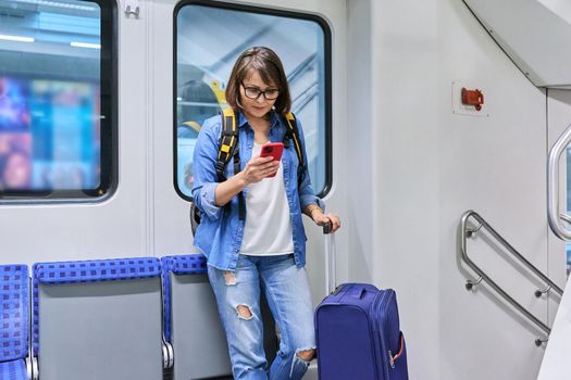 Woman passenger with a suitcase backpack standing inside the car, commuter train. Rail transport, passenger transportation, journey, tourism, travel, trip, people concept