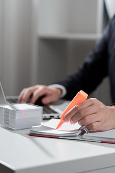 Businesswoman Writing In Notebook And Typing On Lap Top Od Desk With Notes.