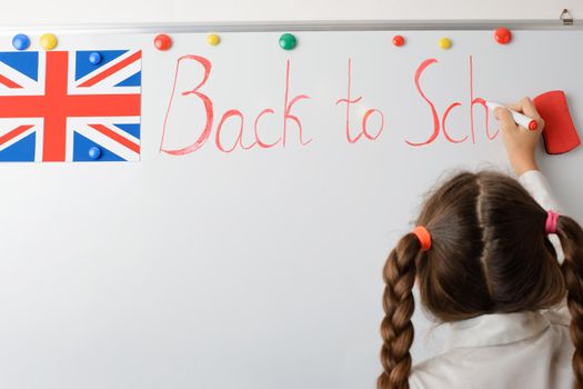 British young learner writing on the board inscription Back to school, happy to return to school after holidays
