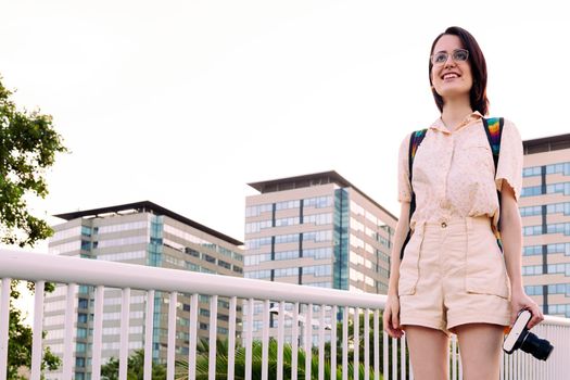beautiful young woman with a camera walking smiling in the city, concept of youth and traveler lifestyle, copy space for text