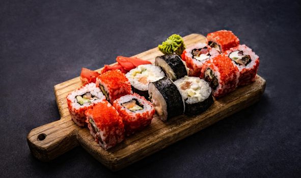 Healthy sushi maki set served on wooden tablet on black table. Beautiful japanese asian roll food composition with prepared rice and seafood