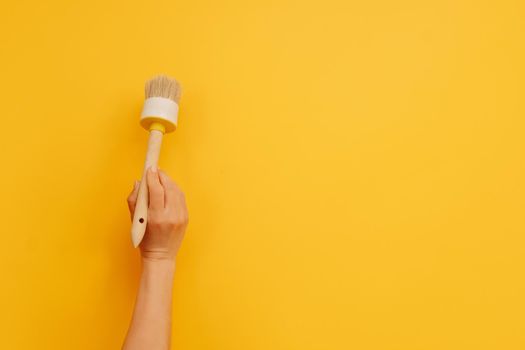 Woman hand holding wooden paint brush on yellow background with copy space. Concept of creativity, improvement and inspiration. Working tool for house design project and improvement