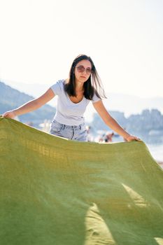Young woman puts a blanket on the pebble beach. High quality photo