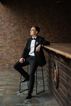 portrait of a young guy groom in a black suit on a rainy day