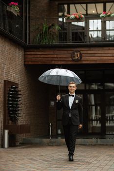 portrait of a young guy groom in a black suit on a rainy day