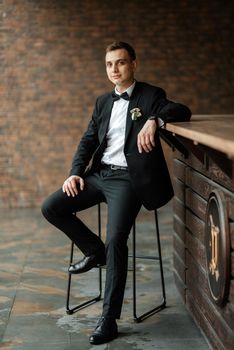 portrait of a young guy groom in a black suit on a rainy day