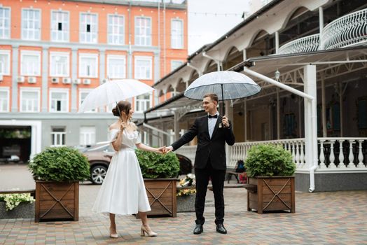 young couple bride and groom in a white short dress walking in the rain