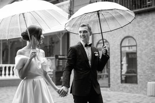 young couple bride and groom in a white short dress walking in the rain