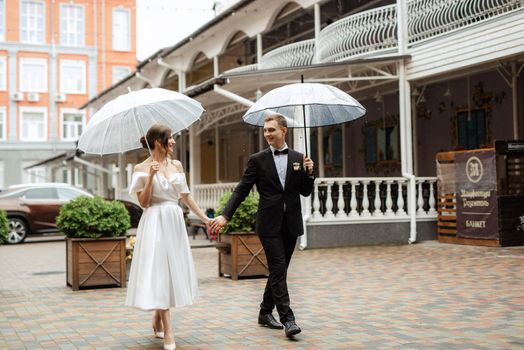 young couple bride and groom in a white short dress walking in the rain