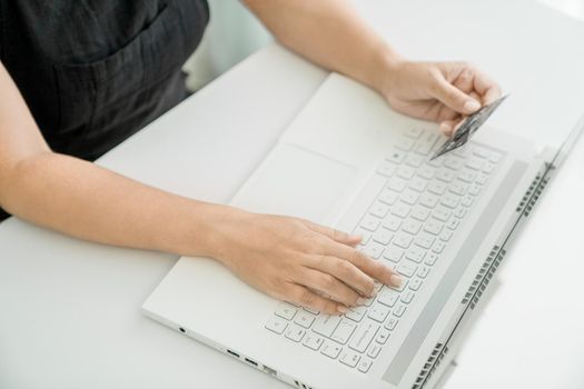 Girl makes online credit card payment via a laptop. Hands close-up. Concept of online shopping and money transfer.