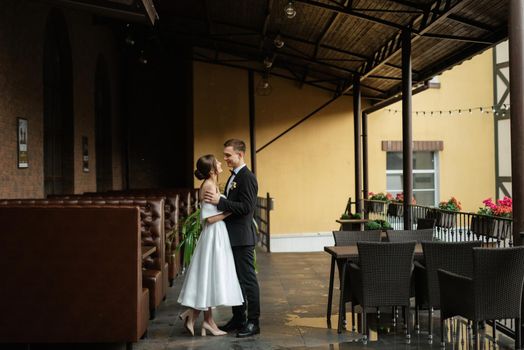 young couple bride and groom in a white short dress walking in the rain