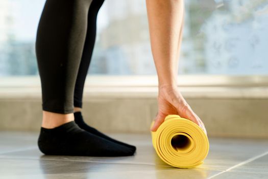 Young woman is preparing to unwrap yellow roll of sports mat for fitness, her hands lie on mat, close-up. Concept of healthy lifestyle.