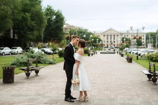 young couple bride and groom in a white short dress walking in the rain