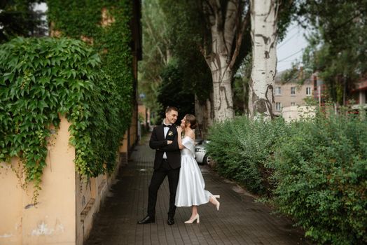 young couple bride and groom in a white short dress walking in the rain