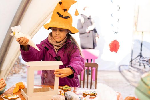 Little kids at a Halloween party. Little girl decorates cookies for Halloween.