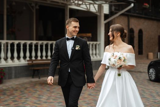 young couple bride and groom in a white short dress walking in the rain