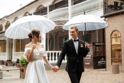 young couple bride and groom in a white short dress walking in the rain