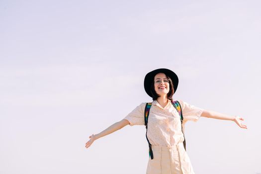 young woman with hat smiling free and happy with open arms in front of clean sky, travel and tourism concept, text copy space