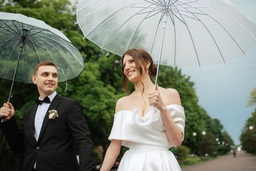 young couple bride and groom in a white short dress walking in the rain