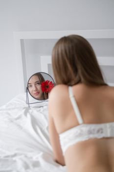 portrait of young woman in underwear on bed. holding red pink flower. female in a hotel room or home. white bedroom and bed sheets bedclothes. happy wonderful day.