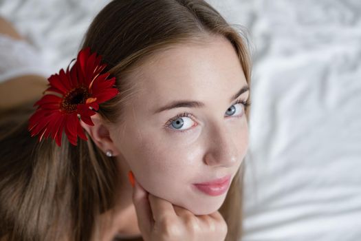 portrait of young woman in underwear on bed. holding red pink flower. female in a hotel room or home. white bedroom and bed sheets bedclothes. happy wonderful day.