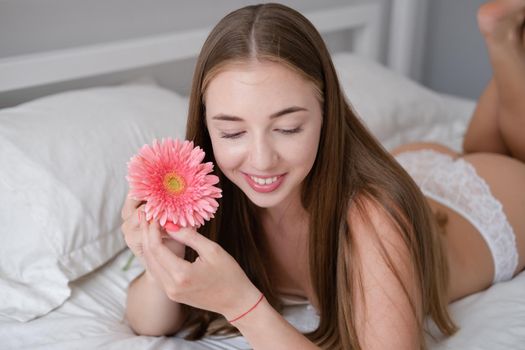 Calm woman with flower lying on her bed. morning routine. successful date. bright white bedroom.