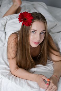 portrait of young woman in underwear on bed. holding red pink flower. female in a hotel room or home. white bedroom and bed sheets bedclothes. happy wonderful day.