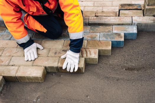 a worker in a protective work suit lays paving slabs. A professional master in work gloves lays paving stones. Paving of the site. Laying paving slabs in the yard of the house on a sandy foundation