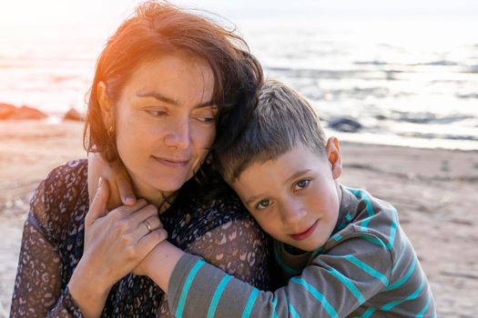 A cute happy preschooler boy hugs his mom on the seashore in the sunset rays. love for parents. Mother's Day