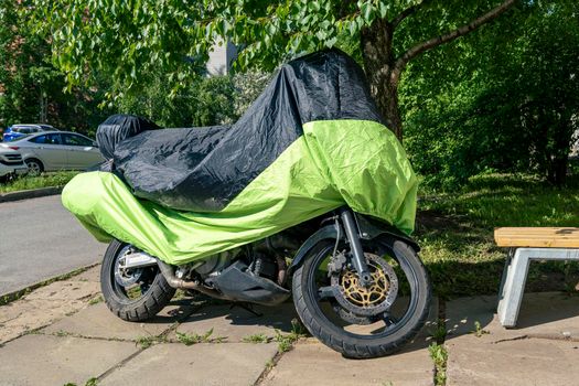 motorcycle in the parking lot in the yard covered with a rain cover. Protective awning for motorcycle