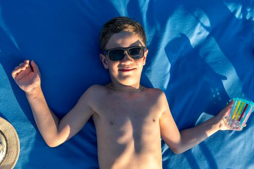 funny happy boy in sunglasses with a bare torso sunbathing lying on the beach. Vacation time, summer holidays