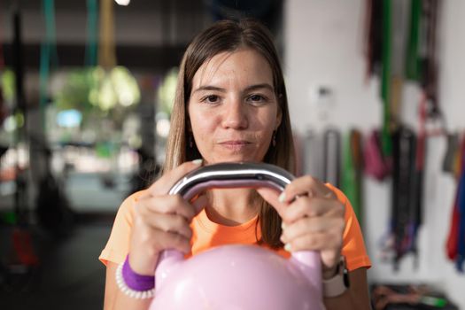 A young woman plays sports and performs exercises holding the kettlebell, at the local training and fitness center