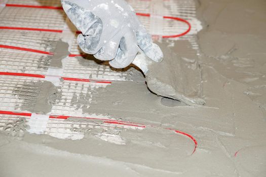 a worker applies cement mortar on an electric cable underfloor heating with a spatula close-up