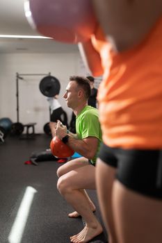 A young man plays sports and performs squats and knee and leg exercises holding the kettlebell, at the local training and fitness center