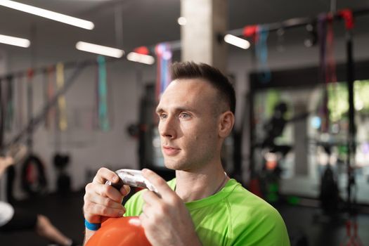 A concentrated young man does sport while holding the kettlebell with his hands, at the local training and fitness center