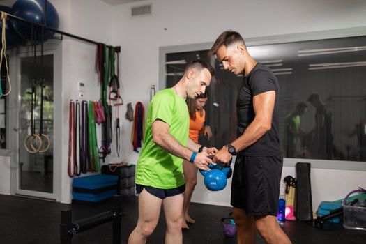 A trainer hands two kettlebell to a young man to exercise at the local training and fitness center