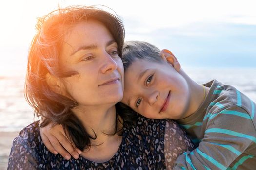 Cute happy preschooler boy hugs his mom on the seashore in the sunset light. love for parents. Close family relationships