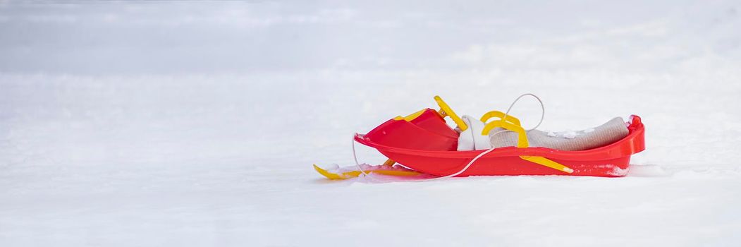 Red sled with snow on a white snowy background. Entertainment in winter for children. Red-yellow plastic sled.