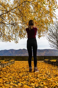 Autumn leaves fallen on alone woman walking on the autumn alley. Autumn landscape, orange foliage in a park in Orsova, Romania, 2020