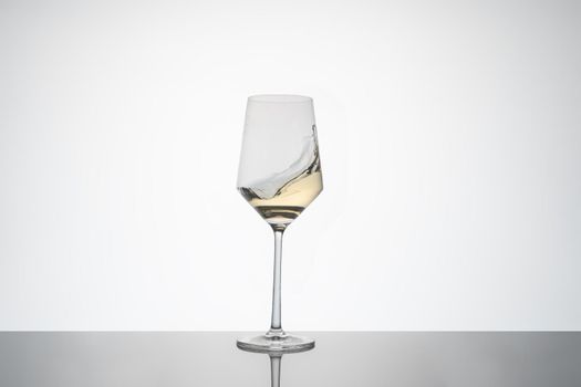 white wine movement inside a crystal glass. white wine glass on white background with reflection on the base. image for cutout. Hard ligth