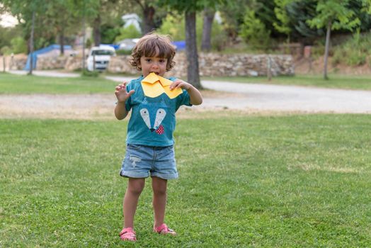 Boy playing toss paper plane outdoors looking away. Portrait of a cheerful caucasian boy playing in the spring and summer park having fun on the weekend