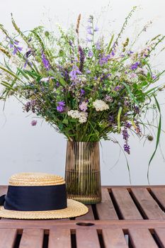 Beautiful wild flowers in bouquet and straw hat on wooden table