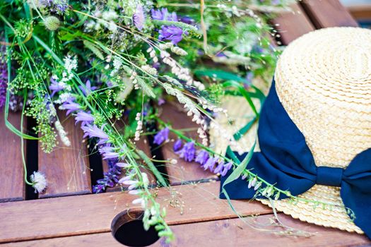 Beautiful wild flowers in bouquet and straw hat on wooden table